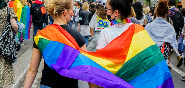 two gen z lgbtq+ women draped in a pride flag