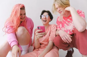 Three LGBTQ+ Gen Z women dressed in pink sitting on the floor and laughing together