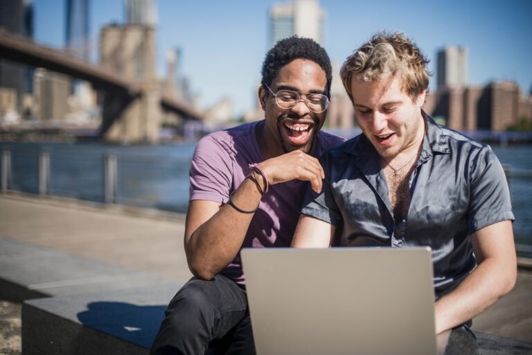 LQBTQ+ Multicultural Gen Z men on a laptop together outside