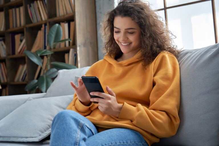 Young Hispanic Gen Z woman sitting on a couch looking at her smartphone