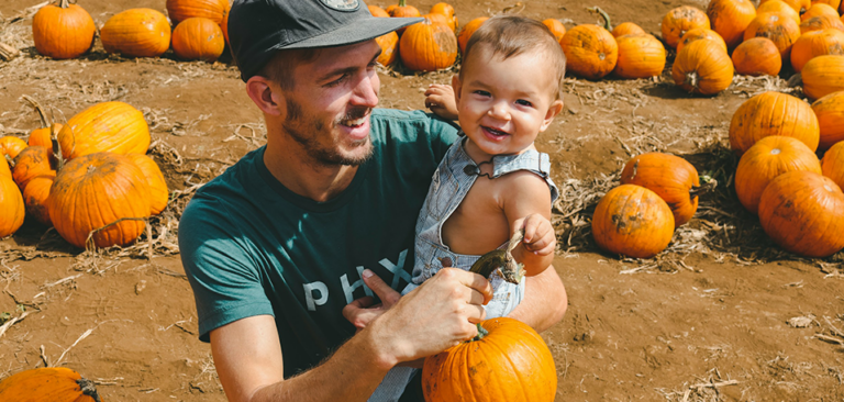Young Gen Z man holding a toddler on his lap in a pumpkin patch