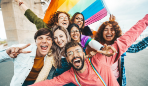 Group of LGBTQ+ Gen Z adults smiling under a pride flag
