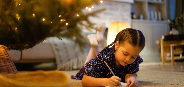 Little girl writing Christmas list under tree