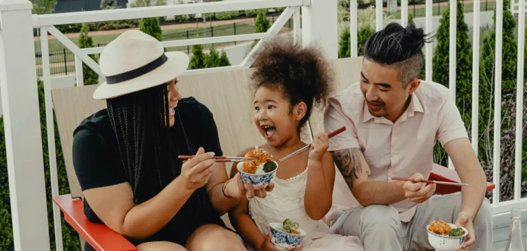 Multicultural family enjoying food outside on a bench